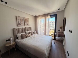A modern hotel room with a large bed, a bedside table with a lamp, a chair, and a view of the outside. - Princess House Maarif (Casablanca)