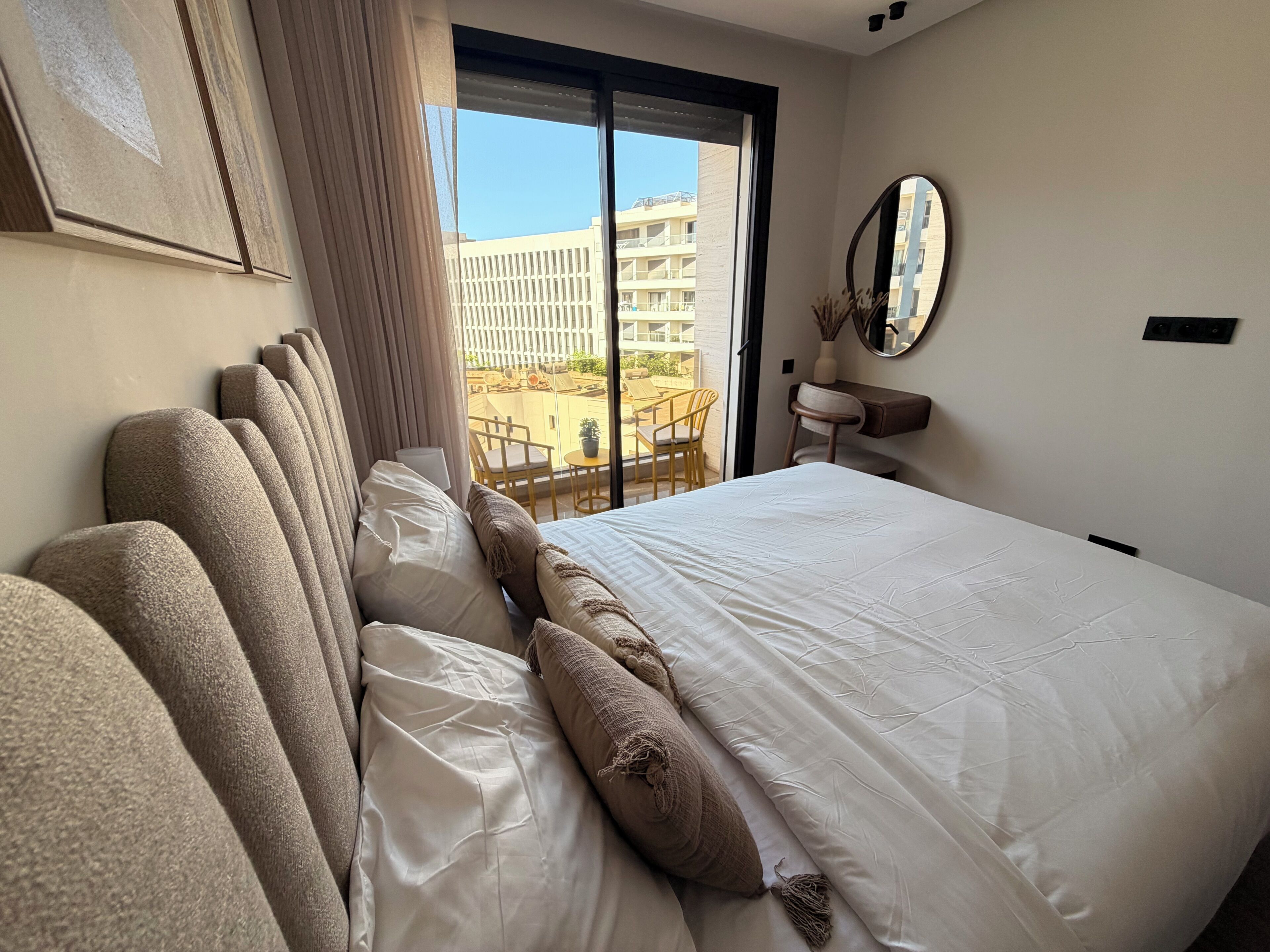 Hotelkamer met een groot bed, een raam met uitzicht op een gebouw, een spiegel en een klein tafeltje met stoelen.