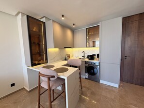 A compact kitchen with a built-in washing machine, a countertop with a sink, and a chair. - Princess House Maarif (Casablanca)