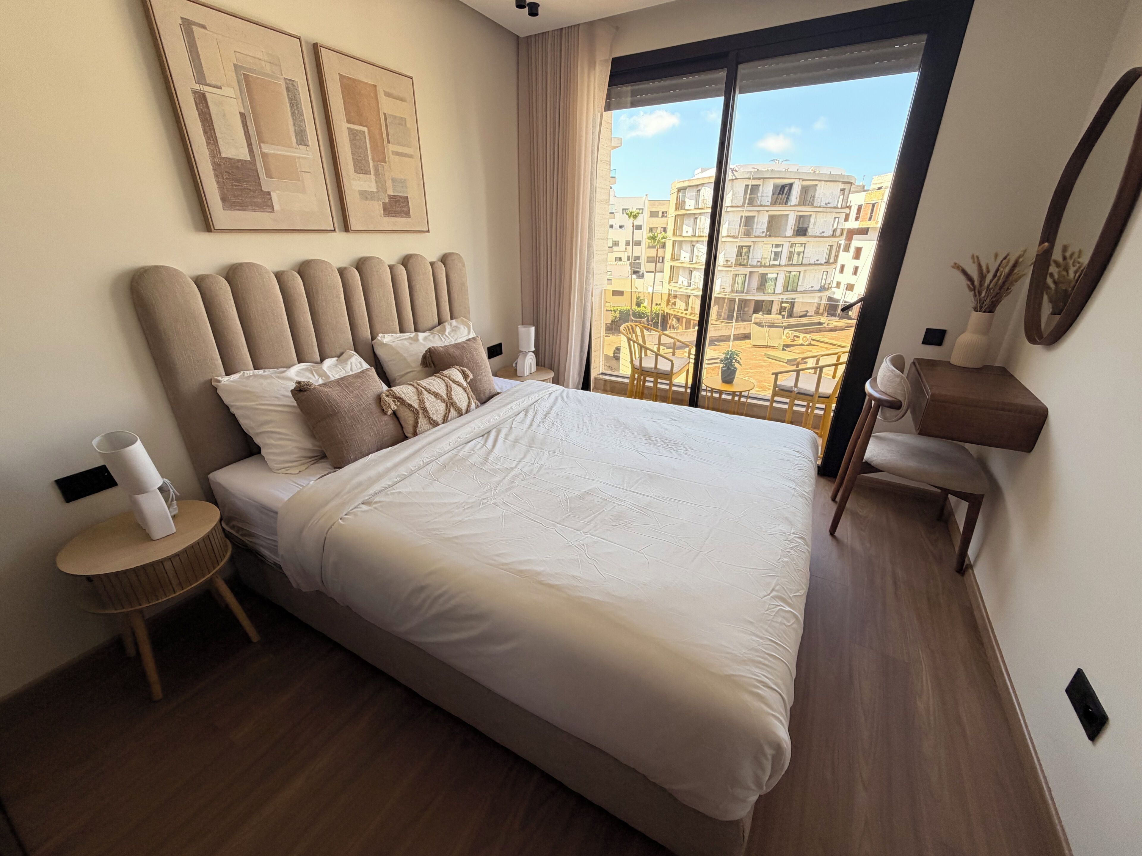 Habitación de hotel moderna con una cama grande, una mesita de noche, una silla y vistas de la ciudad a través de la ventana.
