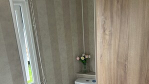 Un baño pequeño con un inodoro, un rollo de papel higiénico y un florero con flores en la pared.