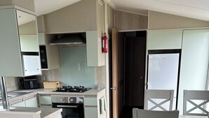 A compact kitchen with a stove, oven, and a microwave. There is a trash bin and a dining area with chairs. - Caravan Sleeps 8 With Sea Views and Parking (Morecambe)