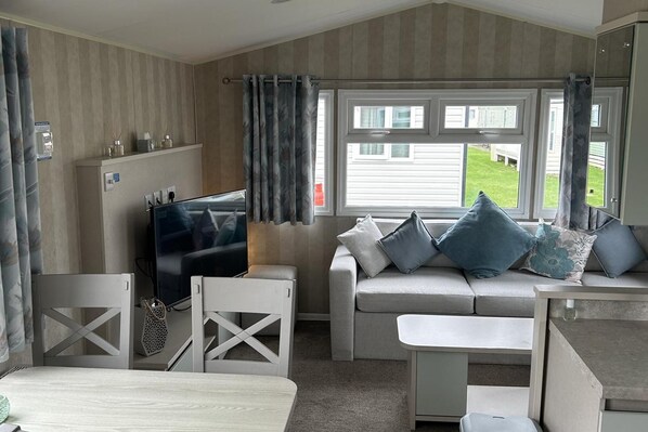 A room with a sofa, a TV, a small table, and a window with curtains.