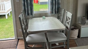 Un comedor con una mesa y sillas, una ventana con cortinas, un refrigerador pequeño y vistas a una propiedad vecina.