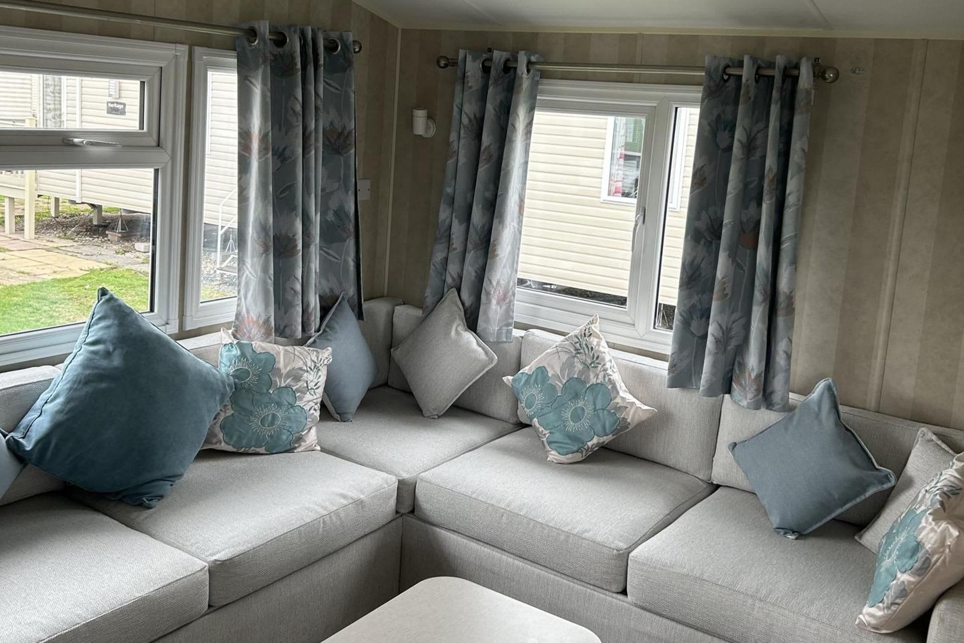 A cozy seating area with a sofa and cushions, large windows with curtains, and a view of the outdoors.