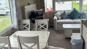 A caravan interior with a dining area, sofa, and a TV. - Caravan Sleeps 8 With Sea Views and Parking (Morecambe)
