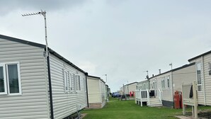 A row of mobile homes with a grassy lawn in between. - Caravan Sleeps 8 With Sea Views and Parking (Morecambe)