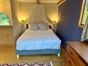 A bedroom with a bed, bedside lamps, a wooden dresser, and a window with a view.