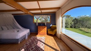 A bedroom with a bed, a dresser, a chair, and a large window with a view of greenery.