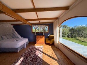 A bedroom with a bed, a dresser, a chair, and a large window with a view of greenery.