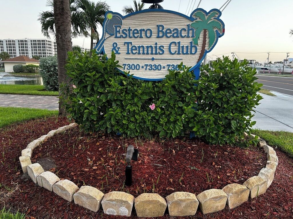 A sign for Estero Beach & Tennis Club with contact numbers.