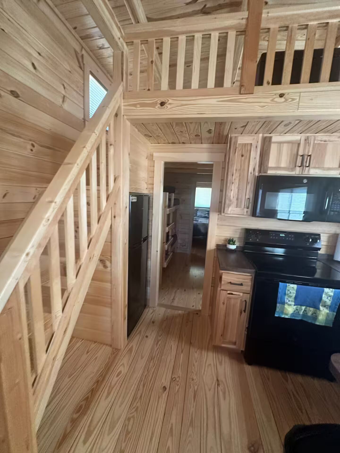 A wooden interior with a kitchen area, including a refrigerator, microwave, and stove.