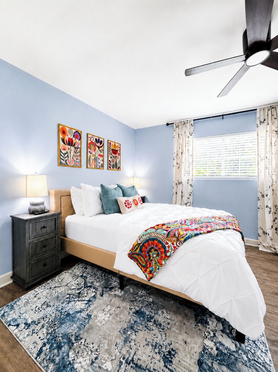 A bedroom with a bed, nightstands, a ceiling fan, and artwork on the wall.