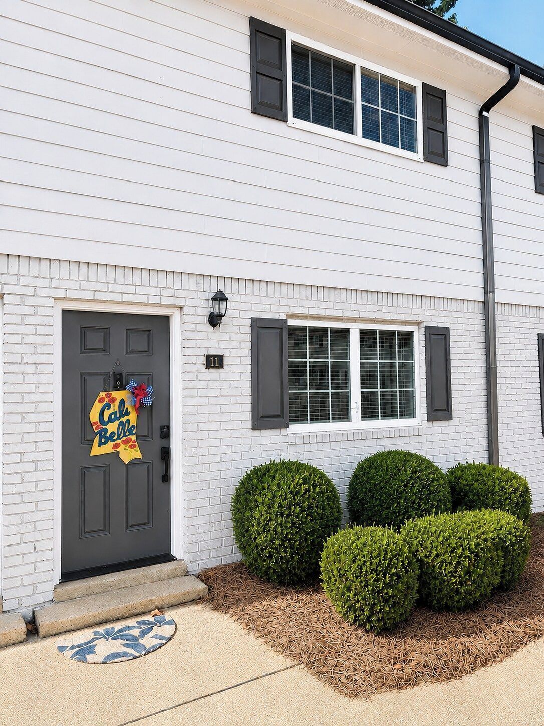A two-story white house with a dark gray door, a small porch, and a mailbox.