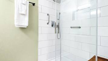 A modern bathroom with a glass shower enclosure, white tiled walls, a wooden bench, and a white towel on a rack.