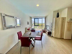 A dining area with a table and chairs, a sofa, a TV, and a view of the outdoors. - Apartment in El Chante Lake View (Chantepec)