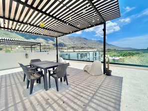 A rooftop terrace with a table and chairs, a pergola with string lights, and a view of mountains. - Apartment in El Chante Lake View (Chantepec)