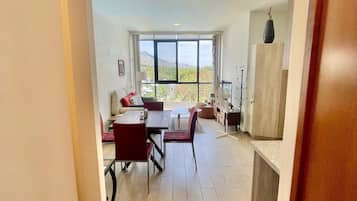 A spacious living area with a dining table and chairs, a sofa, and a view through large windows.