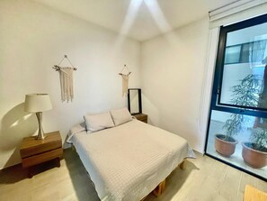 A bedroom with a bed, bedside tables, a lamp, macrame wall hangings, and a window with potted plants. - Apartment in El Chante Lake View (Chantepec)