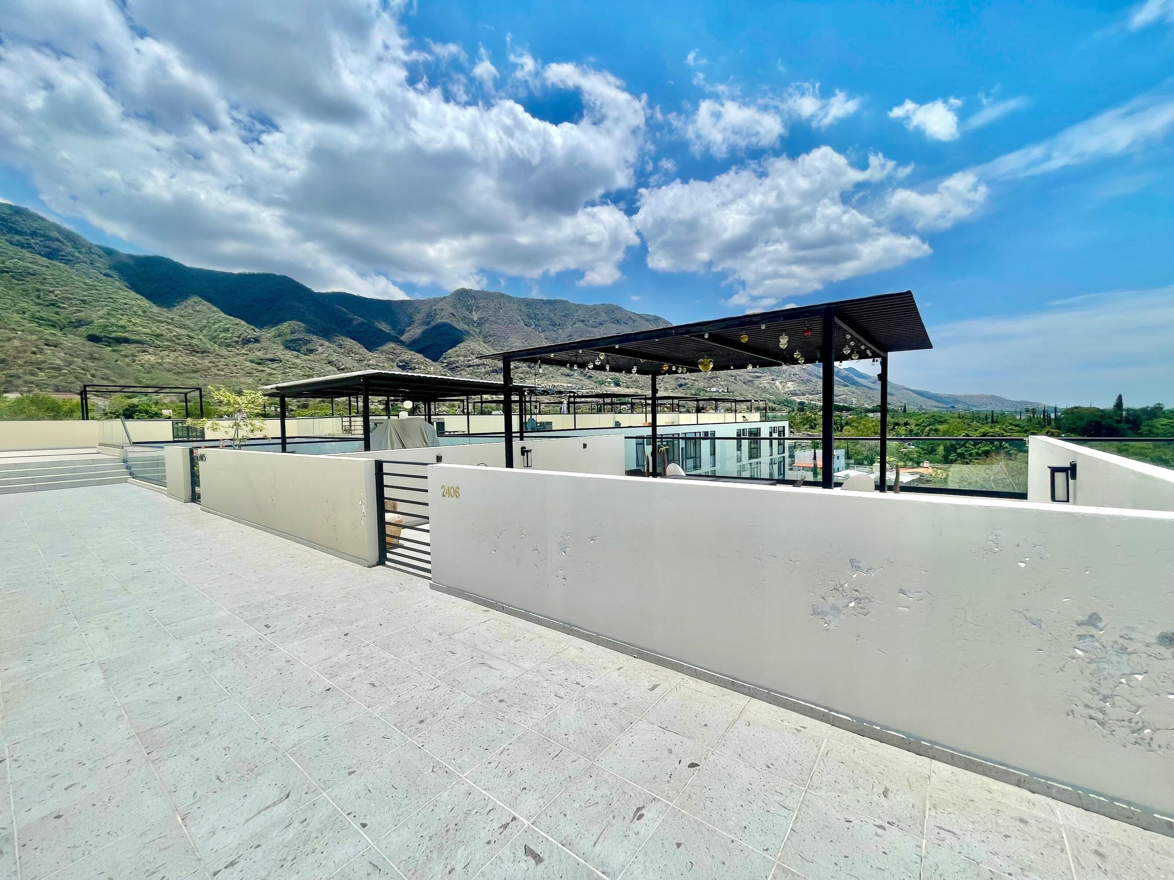 Terraza en la azotea con zona de estar techada, un edificio de vidrio y vistas a las montañas.