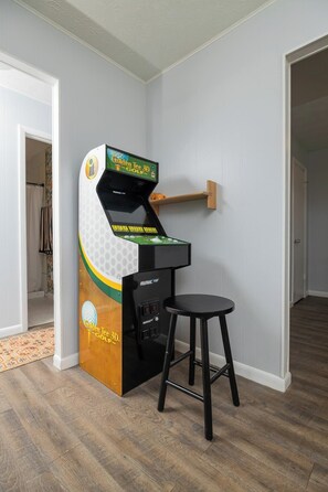 A room with a 3D golf arcade game, a small stool, and a wooden shelf. - Orange Grove home - fully renovated minutes from downtown (St. Augustine)