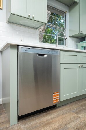 A stainless steel Whirlpool dishwasher in a kitchen with light green cabinets and a window above the sink. - Orange Grove home - fully renovated minutes from downtown (St. Augustine)