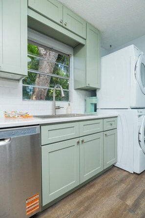 A kitchen with a dishwasher, a washing machine, and a window with a tree view. - Orange Grove home - fully renovated minutes from downtown (St. Augustine)