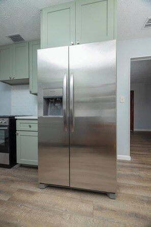 Un refrigerador de acero inoxidable en una cocina con armarios verde claro y salpicadero de azulejos.