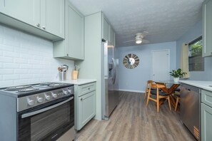 A compact kitchen with a stove, refrigerator, and a dining area with a table and chairs. - Orange Grove home - fully renovated minutes from downtown (St. Augustine)