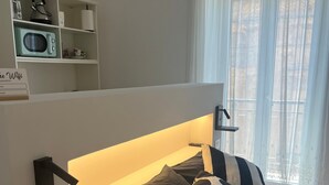 Ein Schlafzimmer mit einem Bett, einer Nachttischlampe und einem Regal mit Wasserkocher und Mikrowelle.