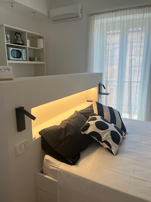 Una camera da letto con un letto, una lampada da comodino e uno scaffale con bollitore e forno a microonde.