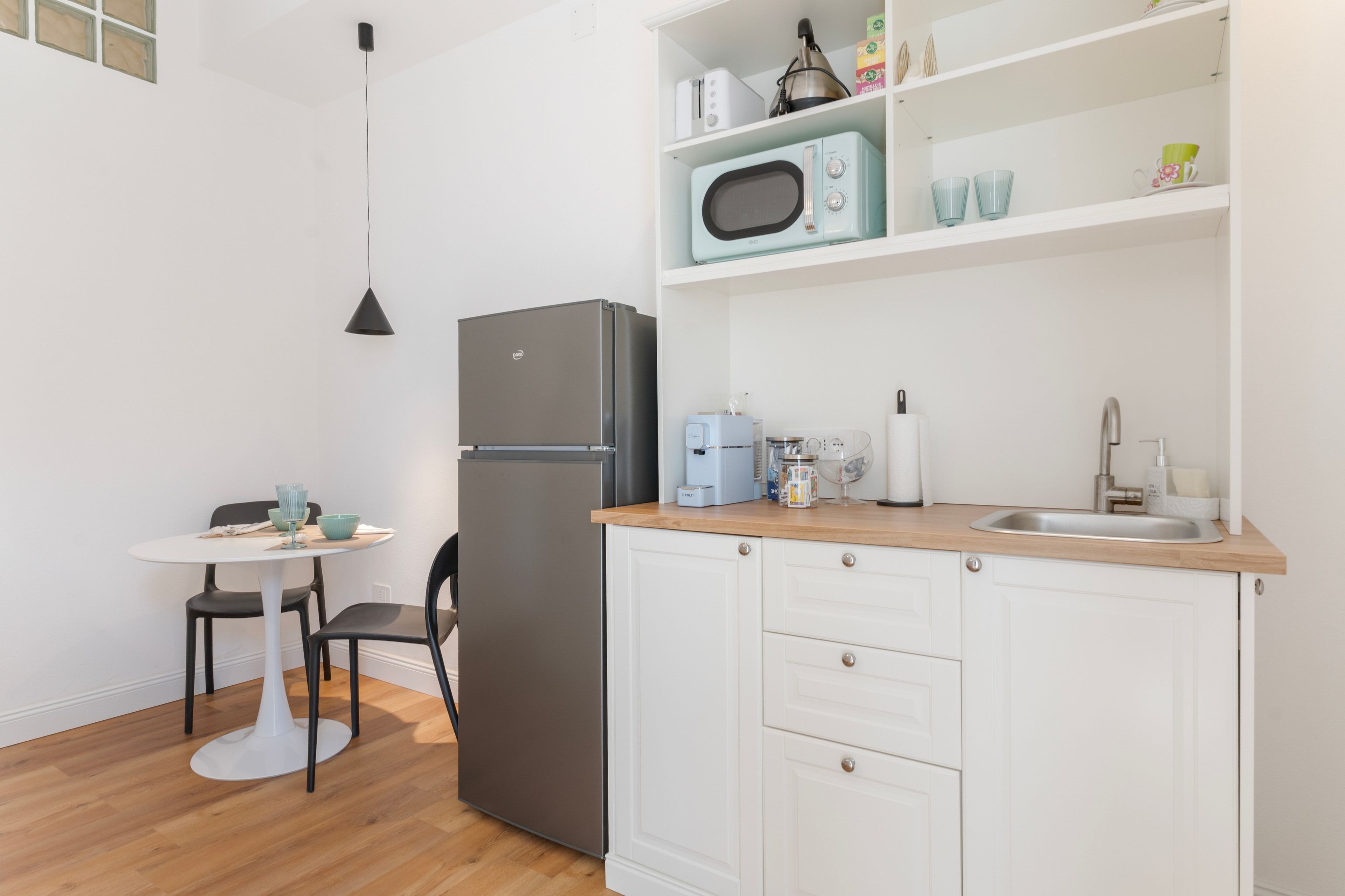 A compact kitchen with a refrigerator, a microwave, a sink, and a small dining area with a table and chairs.