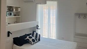 Ein Schlafzimmer mit Bett, weißen Wänden, einem Deckenventilator, einem Fenster mit Vorhängen und einem weißen Kleiderschrank.