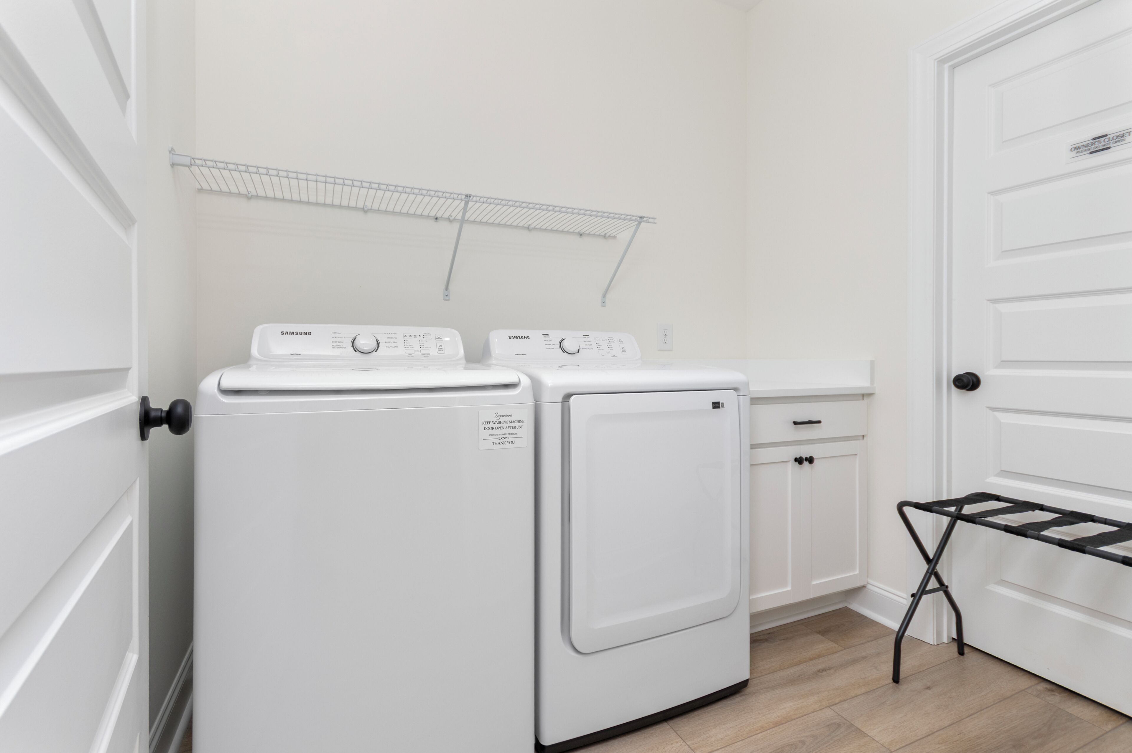 Une buanderie équipée de deux machines à laver Samsung blanches, d’un étendoir et d’une porte blanche avec une pancarte.