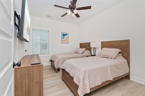 Ein Schlafzimmer mit zwei Betten, einem Deckenventilator, einem an der Wand montierten Fernseher und einem Fenster mit Jalousien.