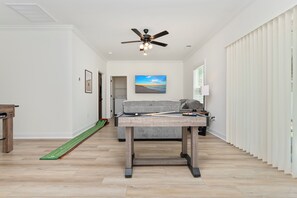 Ein Zimmer mit Pooltisch, Deckenventilator, Gemälde und einem Fenster mit Jalousien.