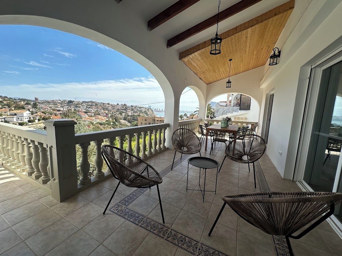 Een balkon met uitzicht op een stad, voorzien van rieten stoelen en een tafel.