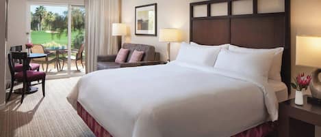 Habitación de hotel con una cama grande, un escritorio con silla, un sofá y vistas a un campo de golf a través de una puerta corrediza.