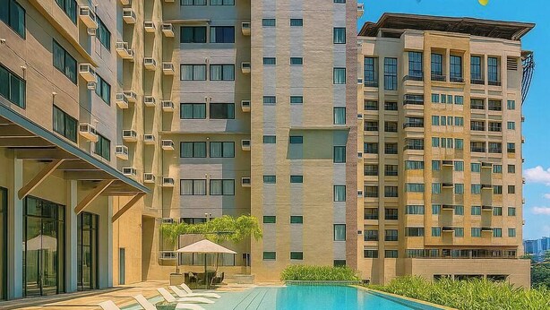 Área de piscina com espreguiçadeiras, piscina e um edifício alto ao fundo.