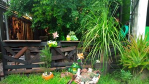 A garden with a wooden fence, various potted plants, a frog statue, and a small wheelbarrow.