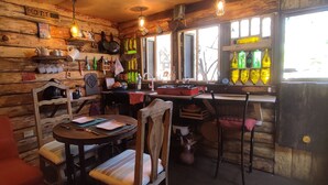 Interior rústico em madeira com área de jantar, bancada na cozinha e diversos utensílios.