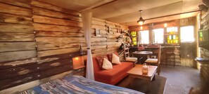 Un interior acogedor con paredes de madera, un sofá, una mesa y una zona de bar con botellas.