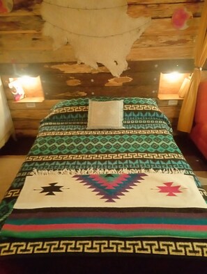 A room with a bed, a hanging decoration, and a small table with a lamp.