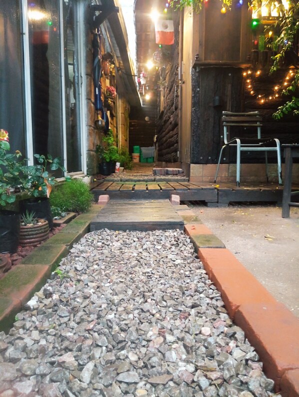 A narrow alleyway with a gravel path, potted plants, and a wooden bench.