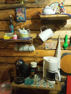 Una cocina con paredes de madera, utensilios de cocina variados, una cafetera y un estante con adornos.