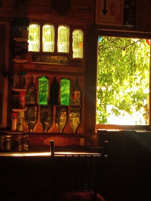 A bar area with a window view of greenery, bottles, and a sign.