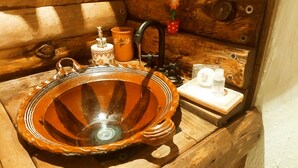 Interior de cabana de madeira com uma pia rústica, um pequeno recipiente laranja e uma flor decorativa.
