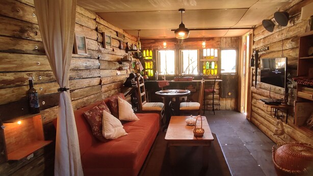 Interior acolhedor de uma cabana com um sofá, uma mesa de jantar e uma televisão.