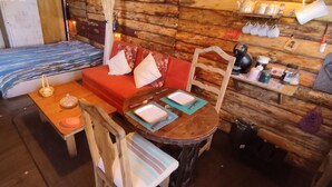 Interior acolhedor de uma cabana, com piso de madeira, um sofá, uma mesinha com uma vela e uma cadeira.