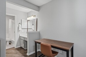 Une petite salle de bain comprenant une douche, des toilettes et un lavabo. Un petit bureau avec une chaise se trouve dans un coin.